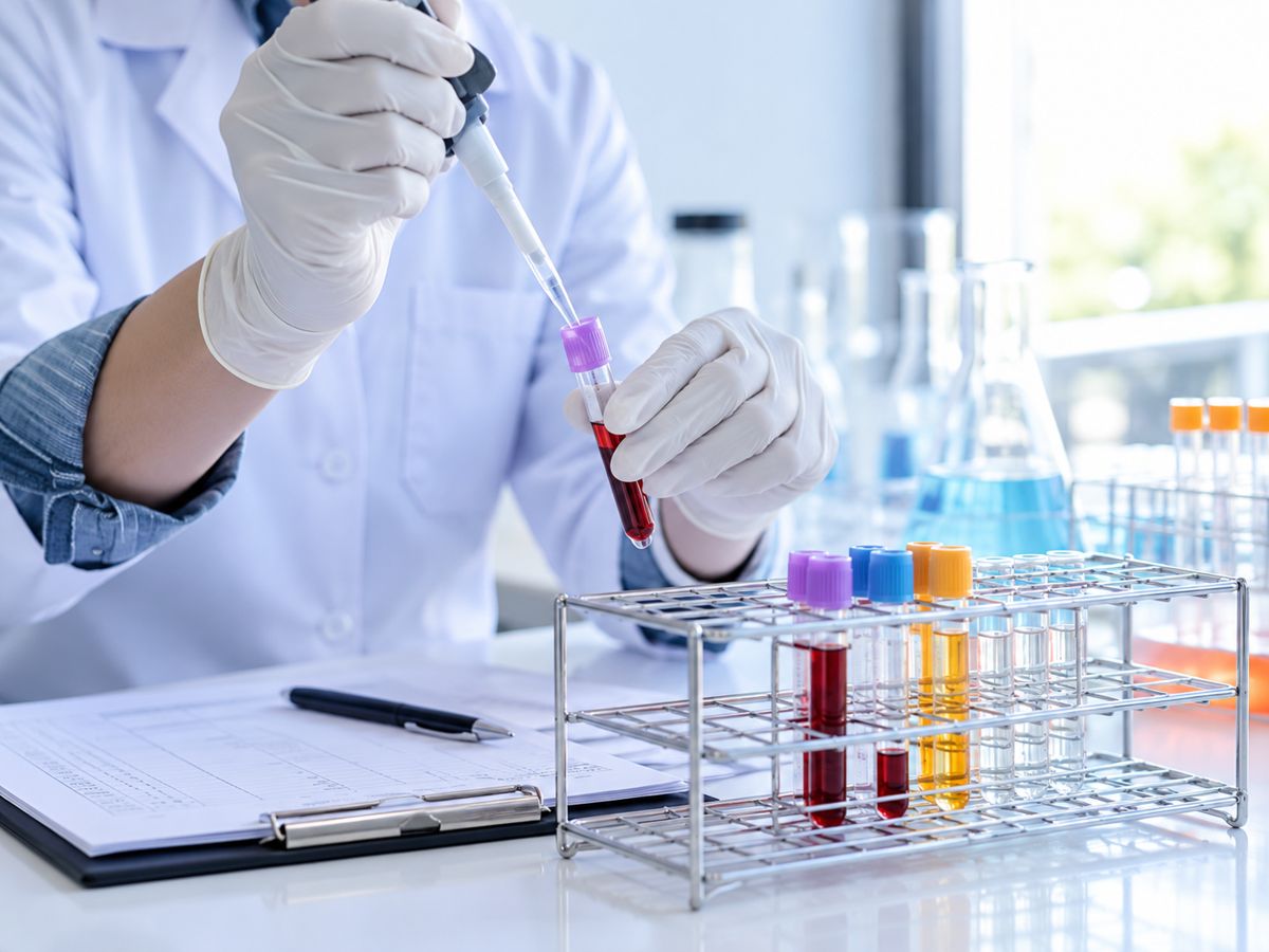 A gloved hand adding a sample to a test tube in a laboratory